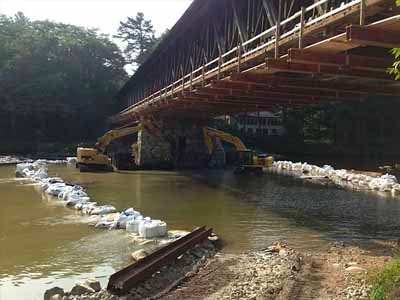 Two excavators working on stone abutment under Blair bridge from the river