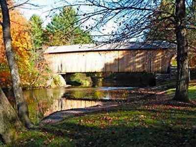 Corbin covered bridge spanning river with autumn foliage reflected in water