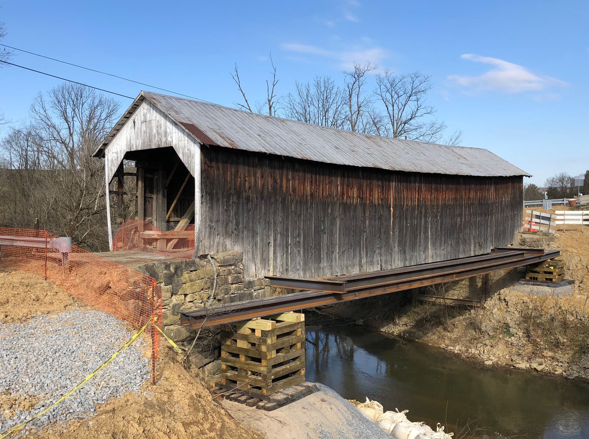 Grange City covered bridge exterior on steel beams over stream with orange construction fencing