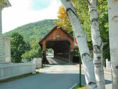 Middle covered bridge exterior viewed from the road with birch trees and village in summer