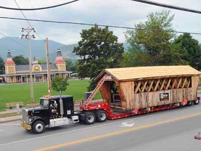 Stoney Morrill covered bridge being transported on flatbed truck through town with mountains in background