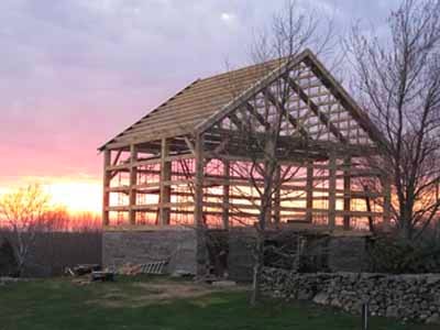 Coleman timber frame silhouetted against sunset with stone foundation walls