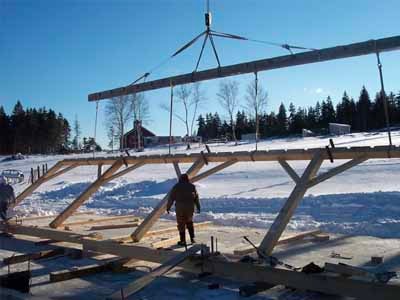 Crane lifting timber truss section at Garner timber frame construction site in winter