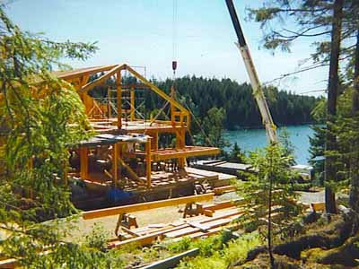 Garner timber frame under construction by lakeside with crane in summer