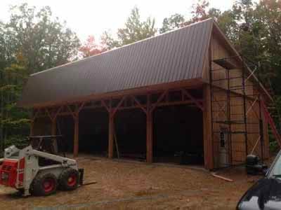 Holderness barn timber frame with brown metal roof and skid steer in foreground
